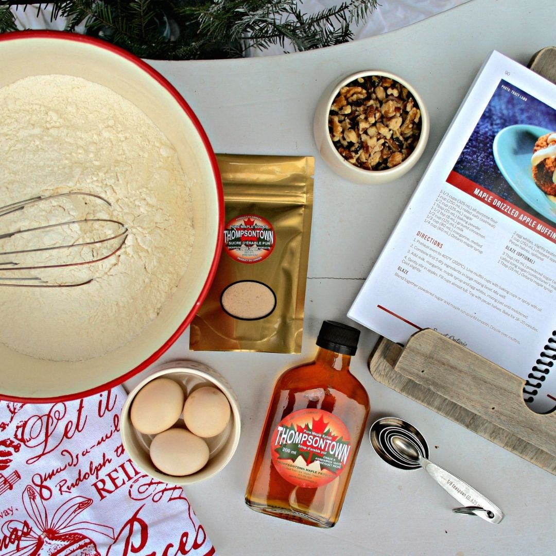 Maple syrup and maple sugar with a mixing bowl, flour, eggs, and recipe book